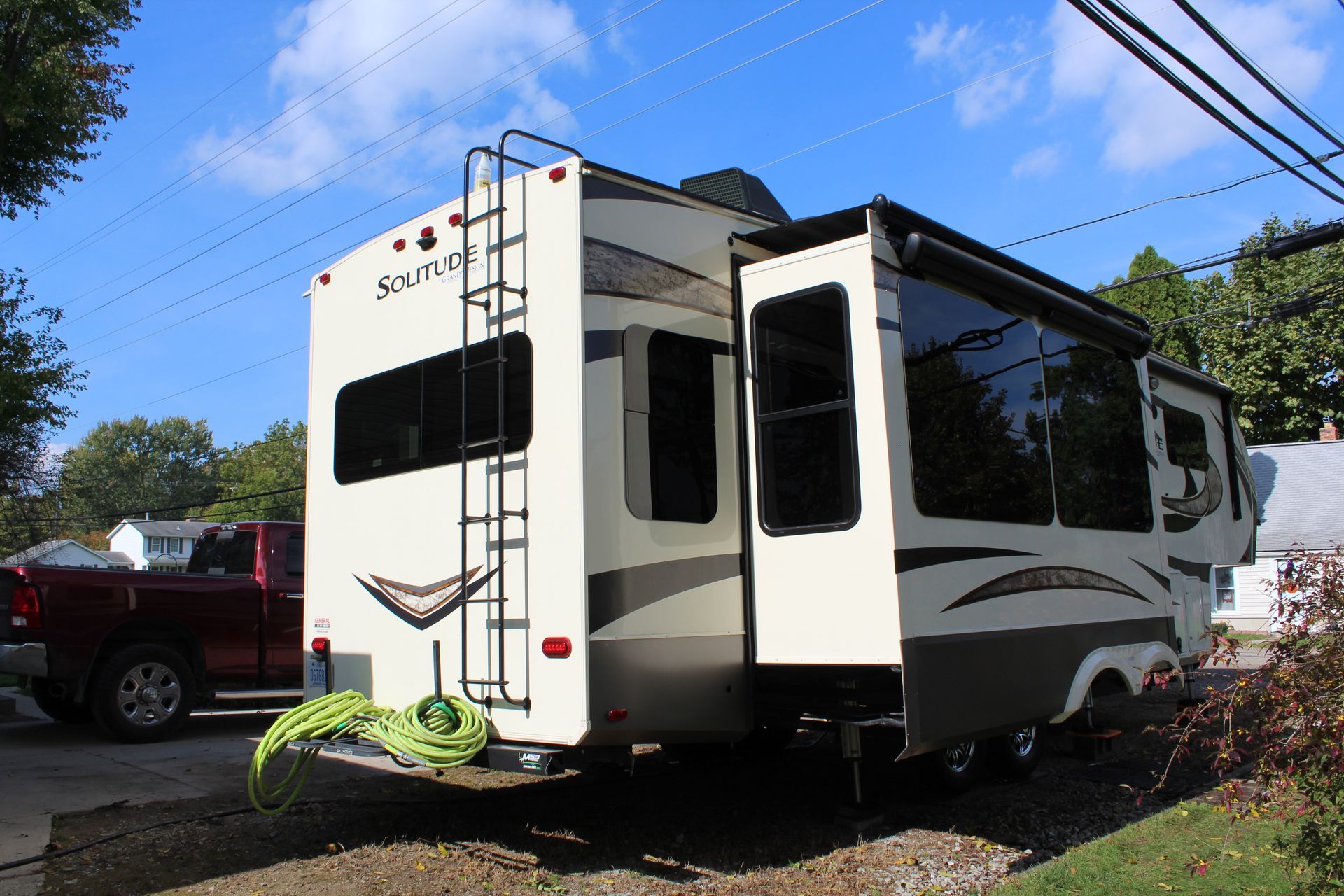 A rv is parked in a driveway next to a red truck.