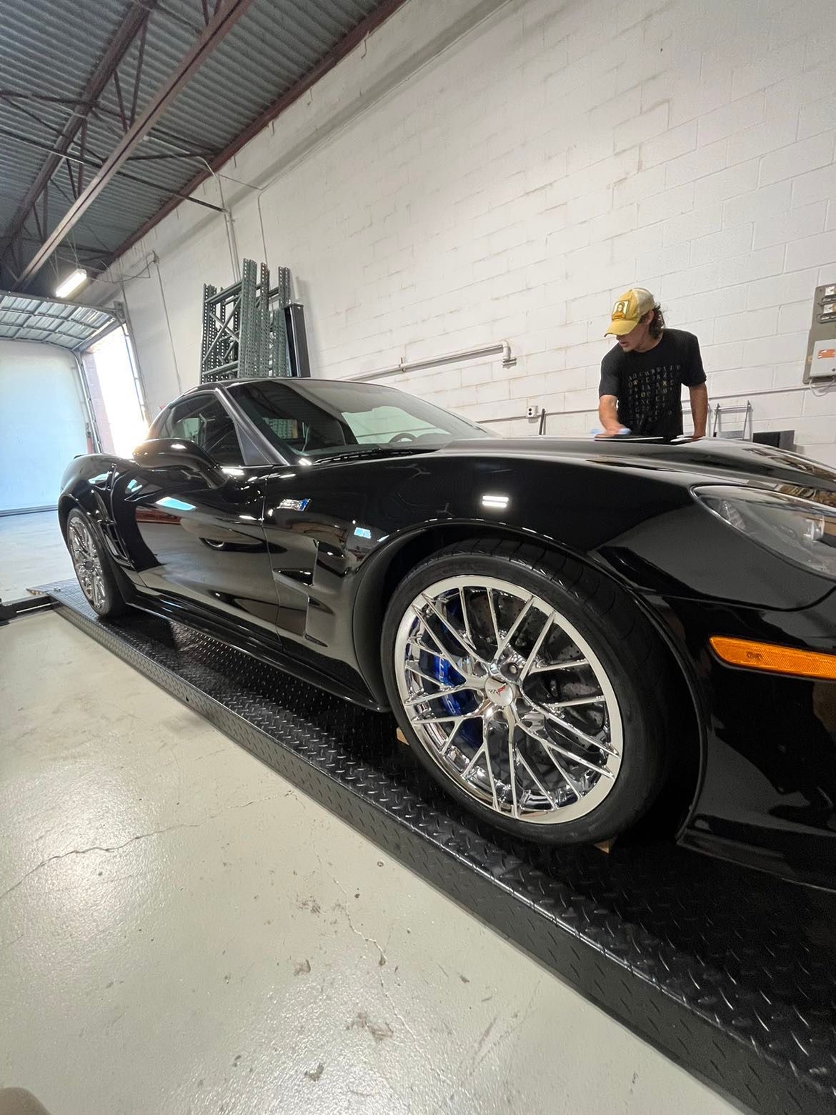 A man is standing next to a black sports car in a garage.