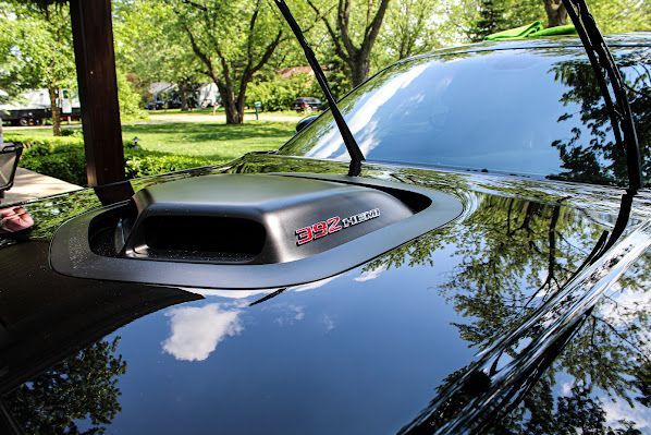 A black car with a hood scoop is parked in a park.