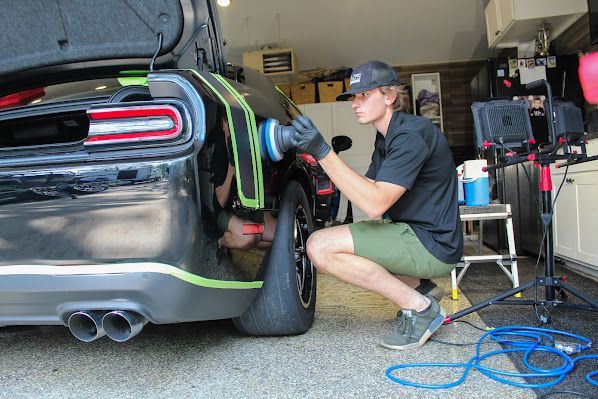 A man is polishing a black car in a garage.