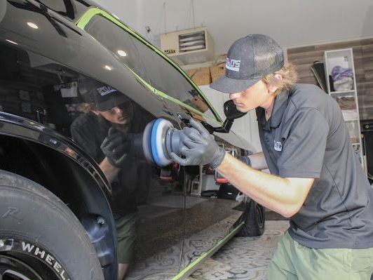 A man is polishing a black car with a machine.