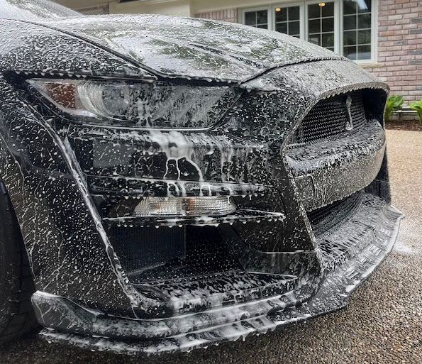 The front of a black car is covered in foam.