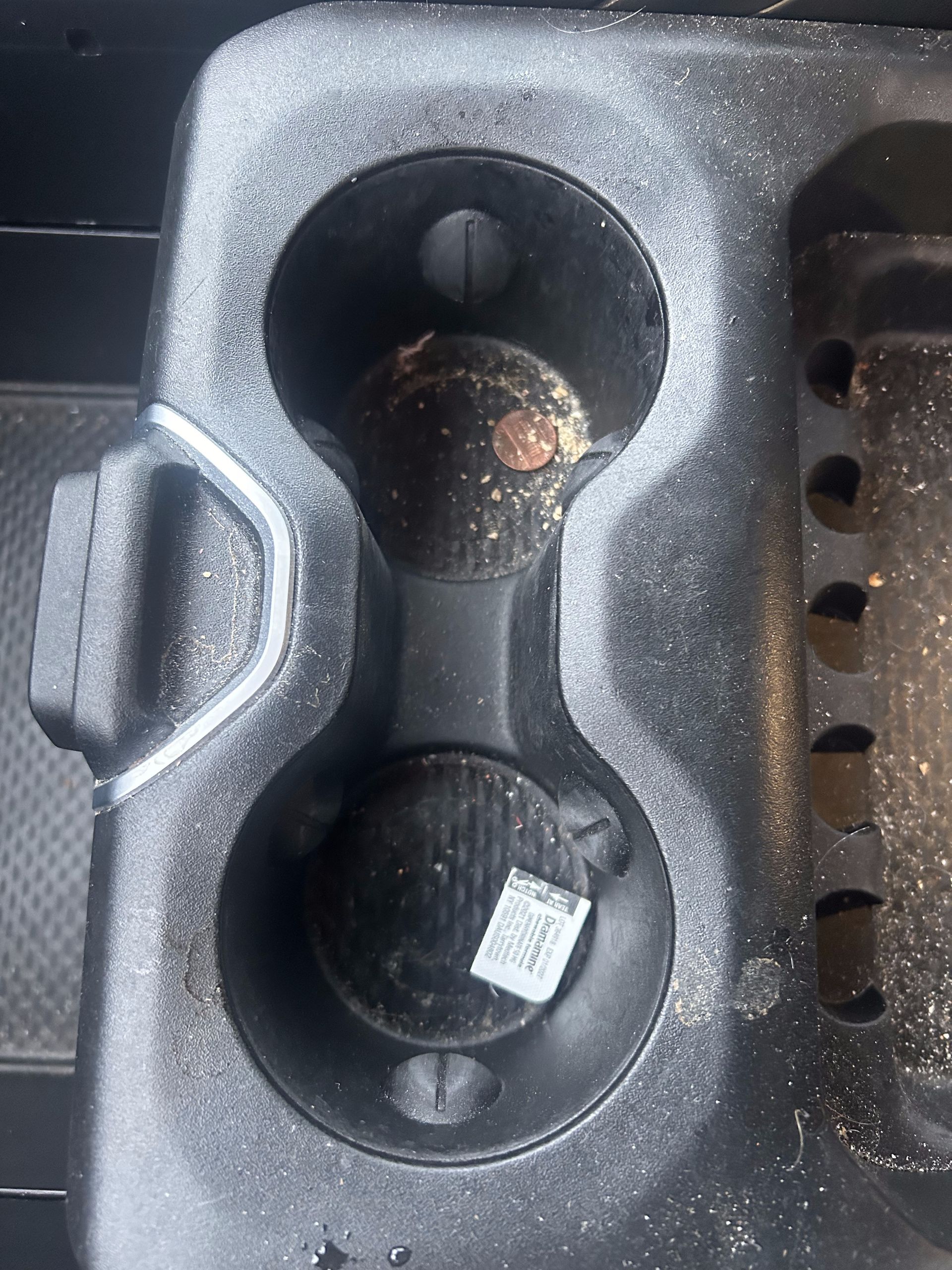 Black car cup holder with two items inside; one appears to be a ball, the other has a sticker.