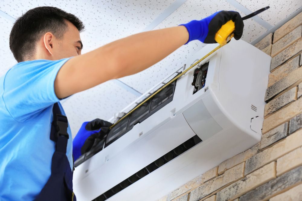 Male Technician Using Measuring Tape To The New Air Con Installed — John B Electrical In Beechworth VIC