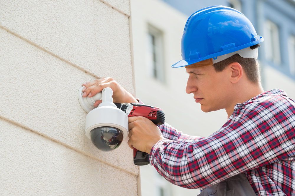 Male Technician Installing Camera On Wall Using Electric Cordless Drill — John B Electrical In Beechworth VIC