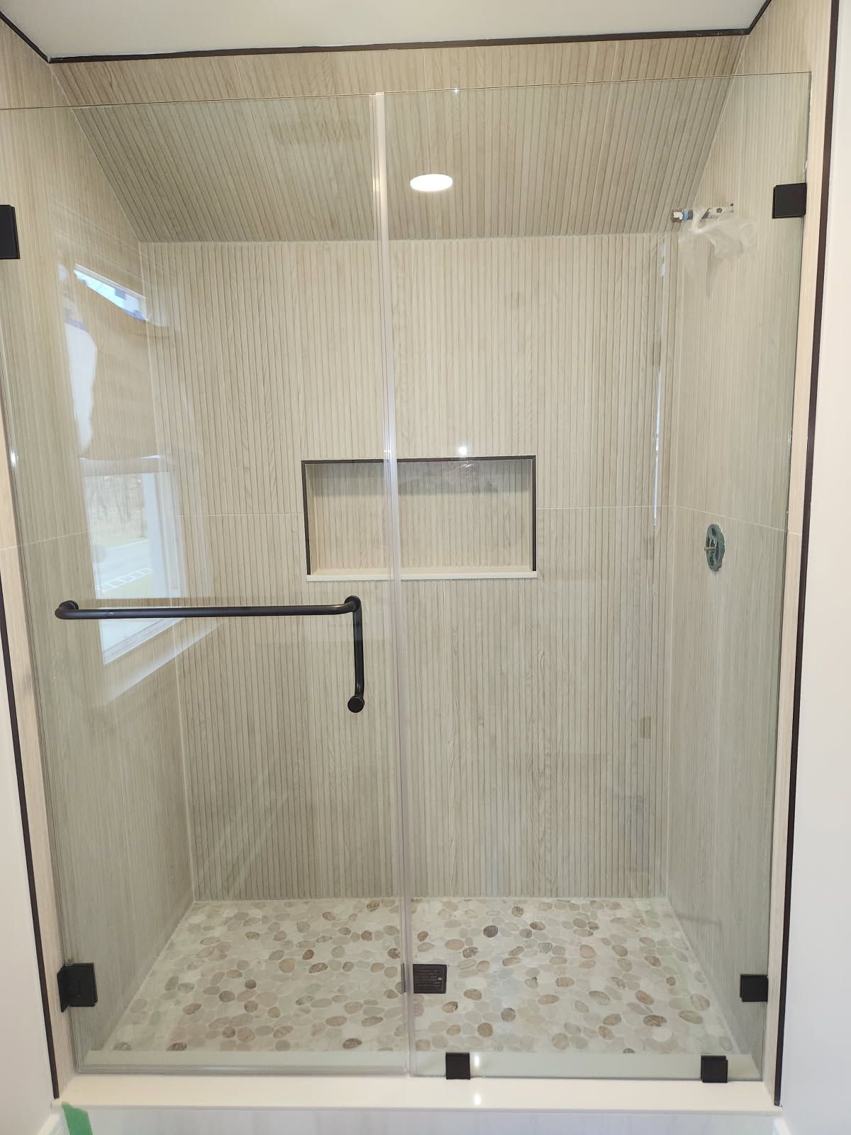 A shower stall with a glass door and a black handle.
