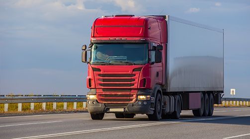 Red semi-truck hauling a white trailer on a highway under a clear sky.