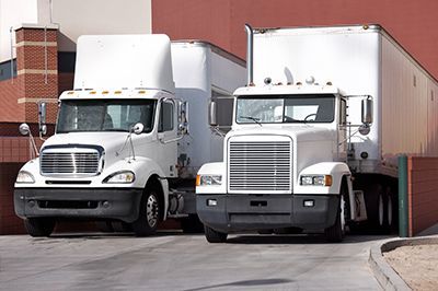 Two white semi trucks parked side by side beside a brick building