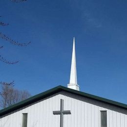 White church steeple with a cross against a bright blue sky.