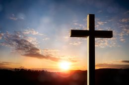 Cross silhouetted against a sunset with orange and blue sky.