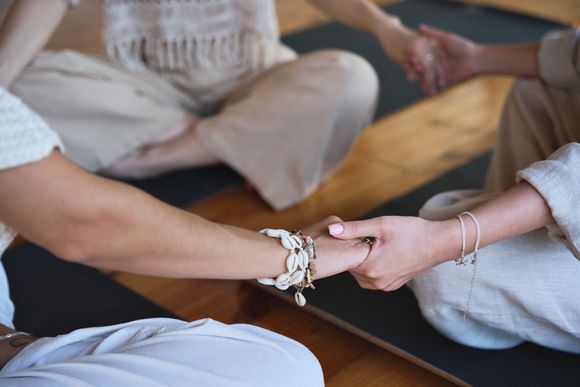 Two people seated on a mat holding hands in a calm indoor setting