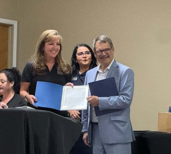 Woman and man holding certificates; smiling in an office setting. A woman in black shirt stands between them.