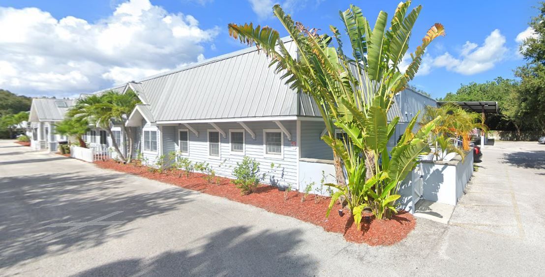 A light blue building with a metal roof, palm trees, and red mulch. Exterior shot.