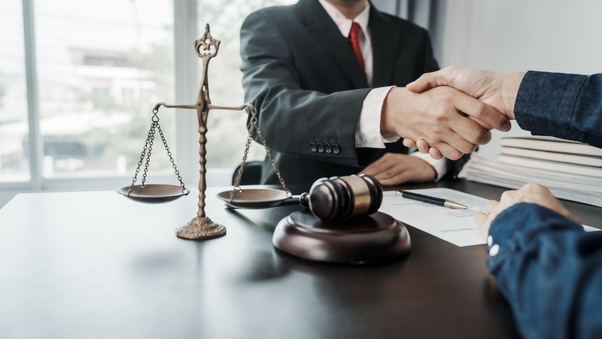 Handshake over a legal desk with a gavel, scales of justice, and stacked documents