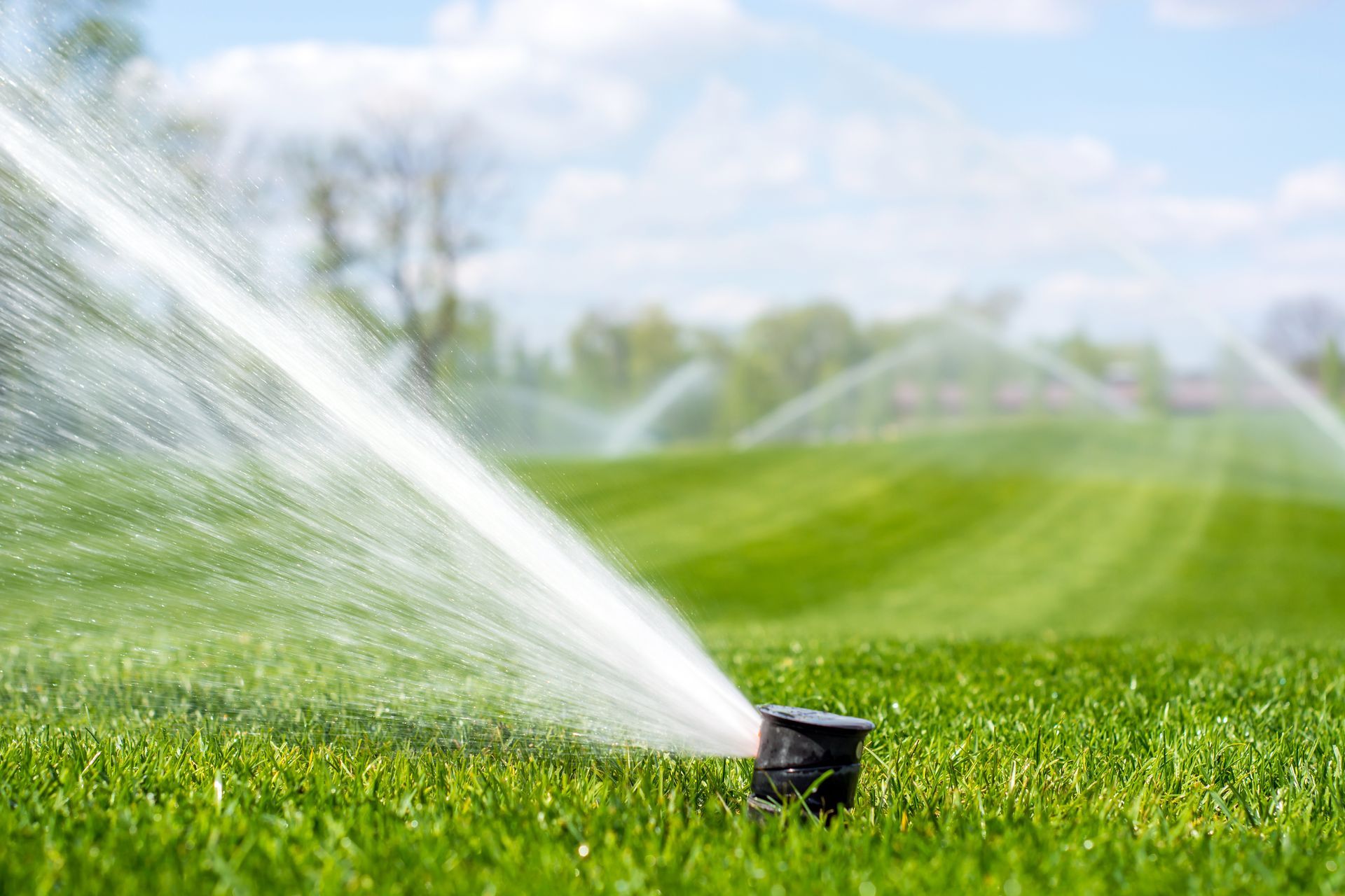 A lawn sprinkler spraying water across a vibrant green field under a clear blue sky.