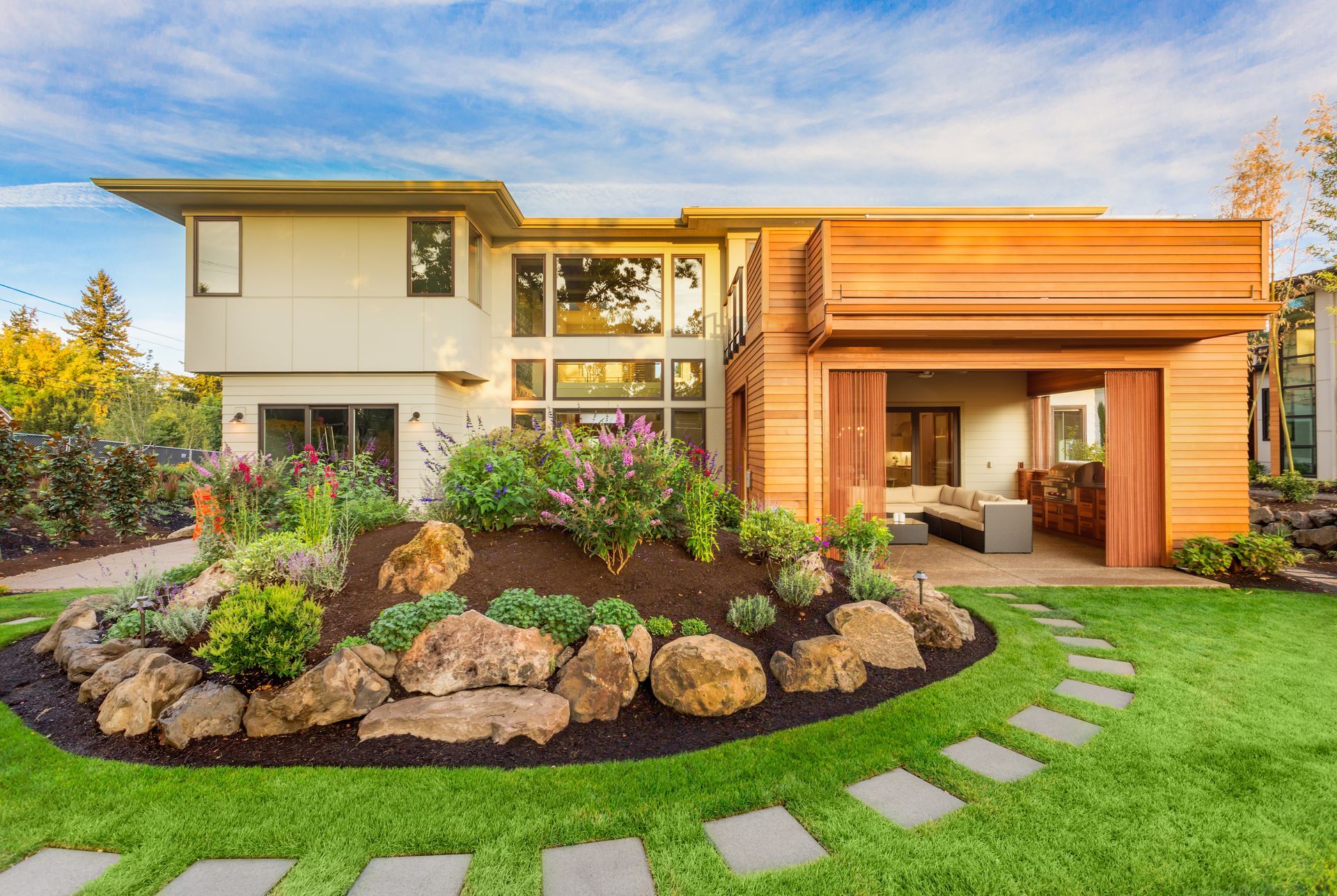 A modern two-story home with a wood-paneled patio and a curved stone pathway leading through a landscaped garden.