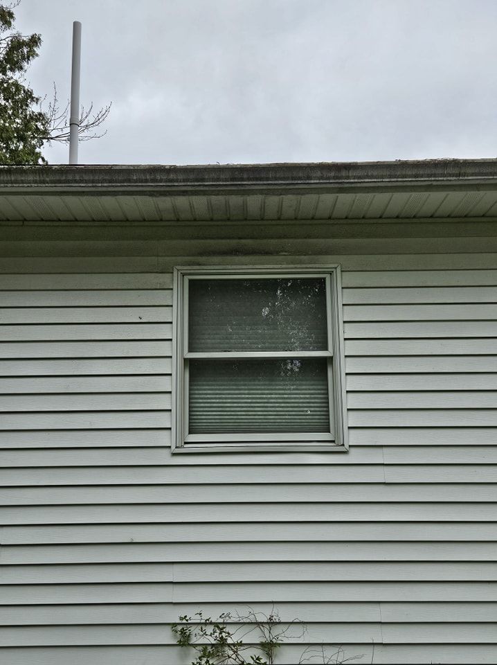 A light-colored house exterior with horizontal vinyl siding and a centered rectangular window under an overhanging eave.
