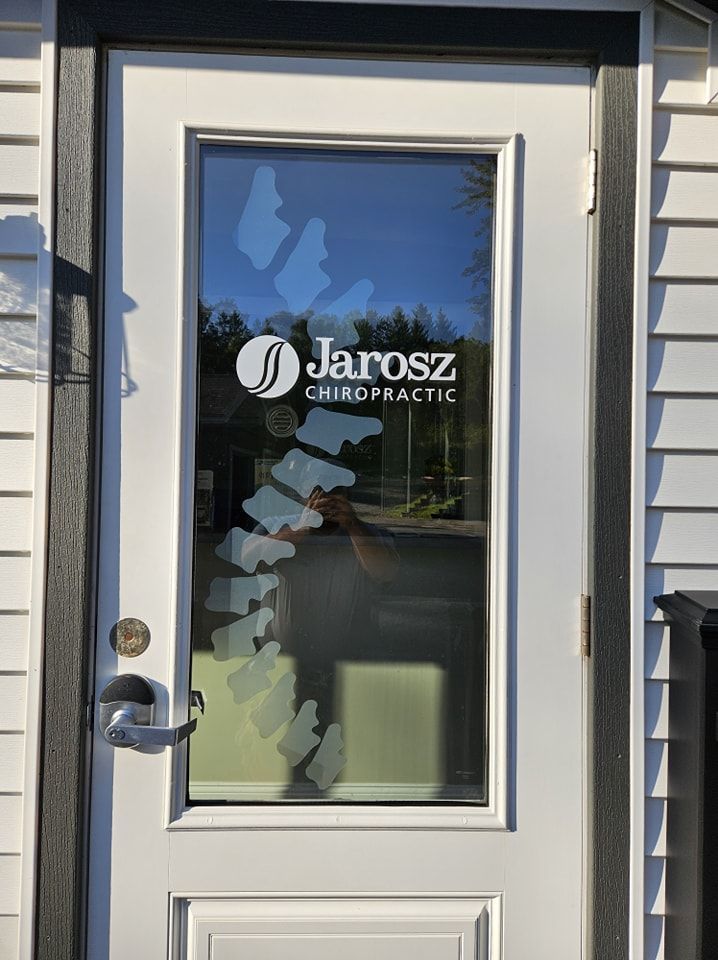 White exterior door with a glass pane displaying the Jarosz Chiropractic logo and a frosted decal of a human spine.