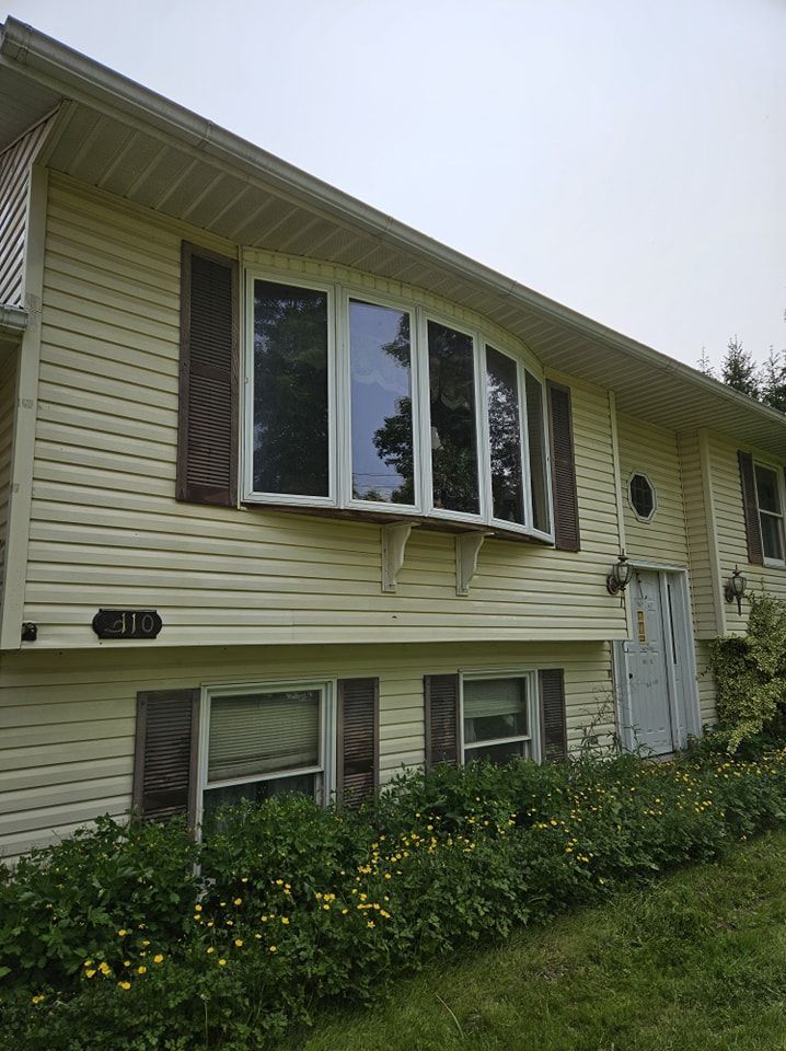 A yellow-sided split-level home with a large bay window, dark brown shutters, and a front flower bed.