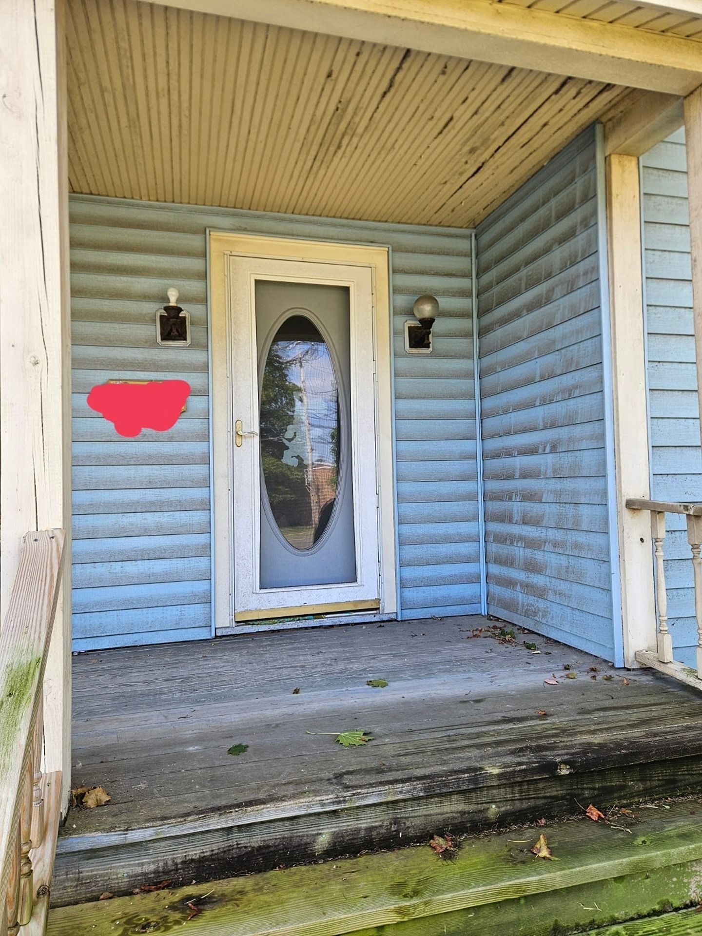 A light blue house front porch with a white storm door featuring an oval glass pane and two exterior wall lights.