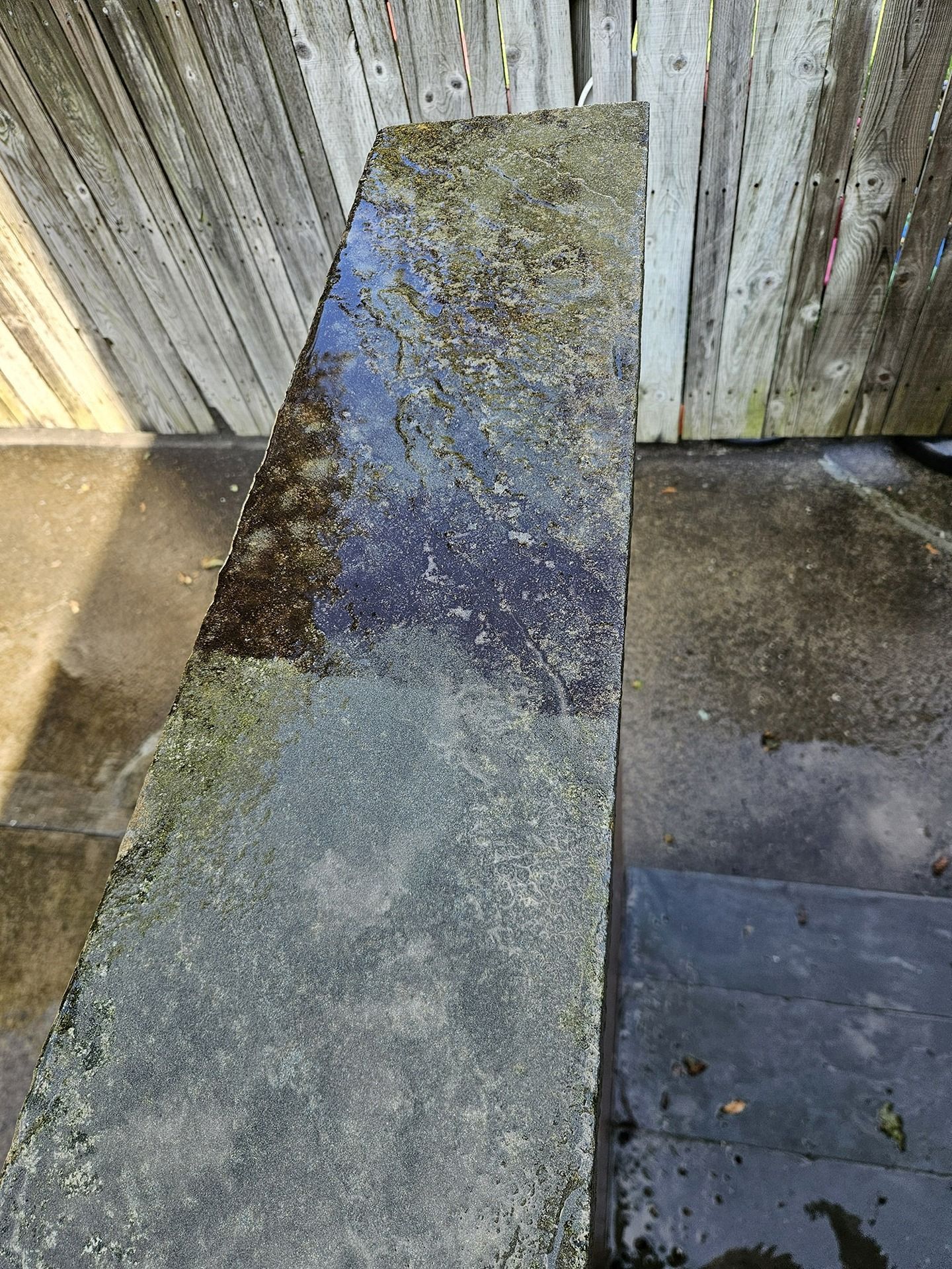 A high-angle view showing a comparison of a dirty stone ledge next to a recently cleaned, dark, wet section.