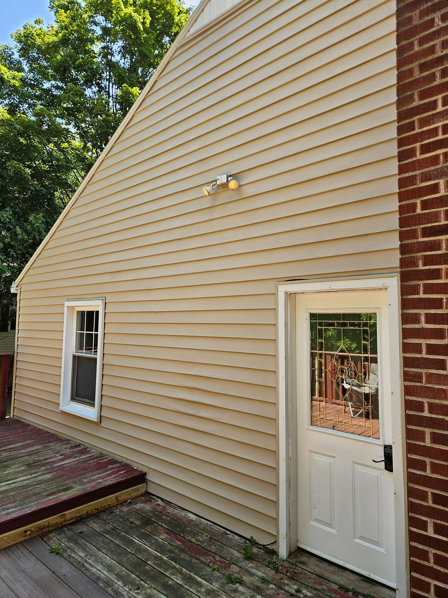 Tan vinyl siding on the exterior of a house, featuring a white door, a small window, and a weathered wooden deck.