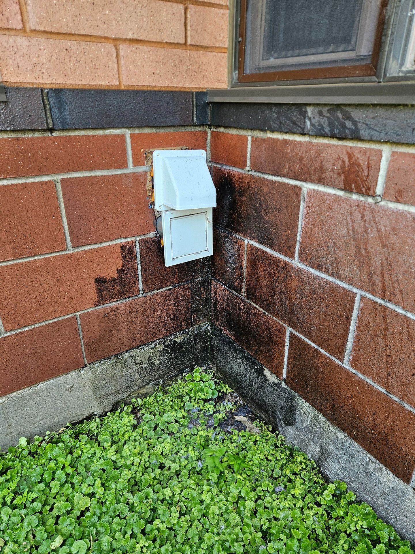 A dryer vent on a brick house exterior showing dark staining from lint accumulation on the surrounding bricks.