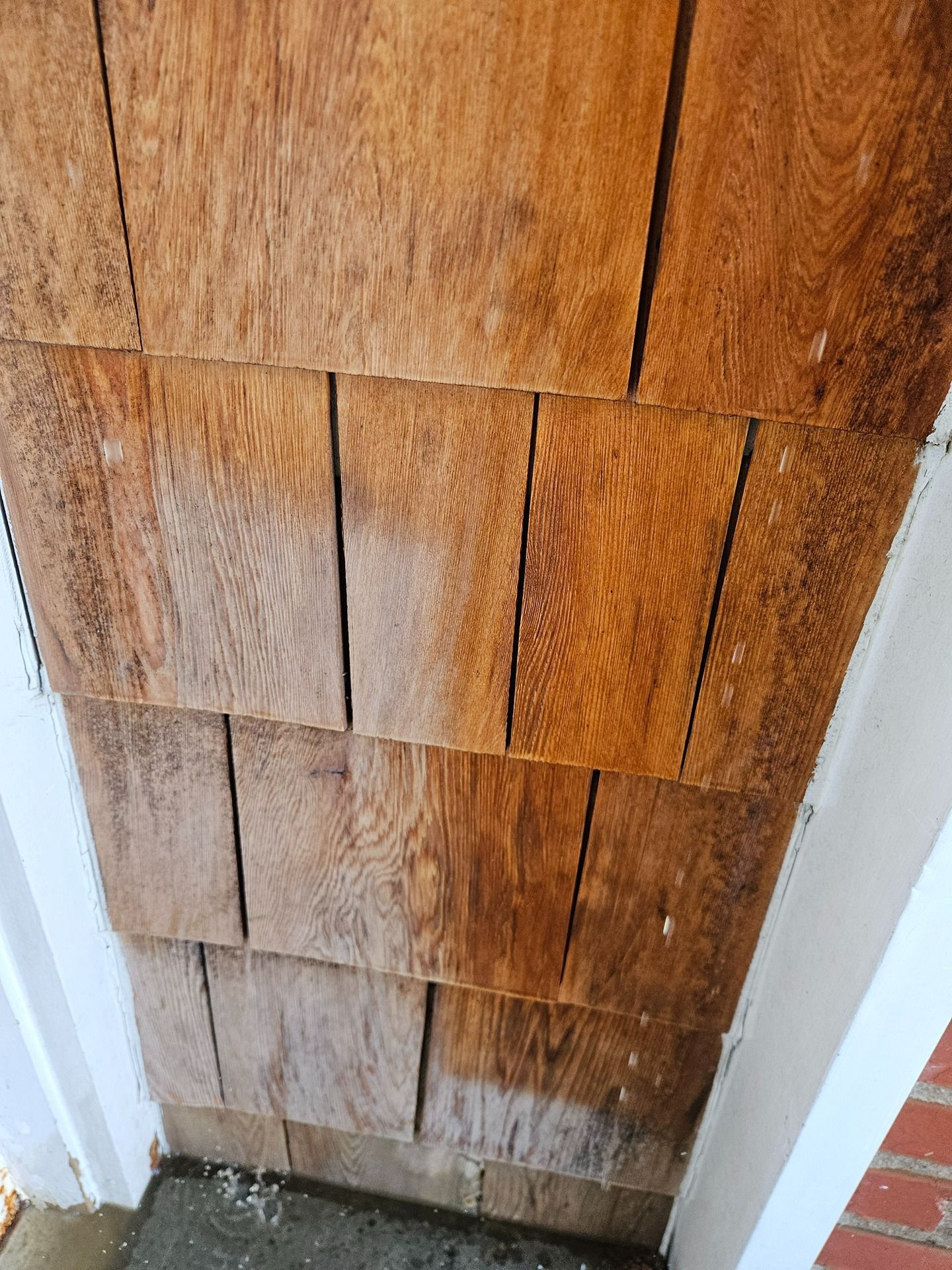 A close-up view of light brown wooden shingles on a house exterior, showing variations in tone and texture.