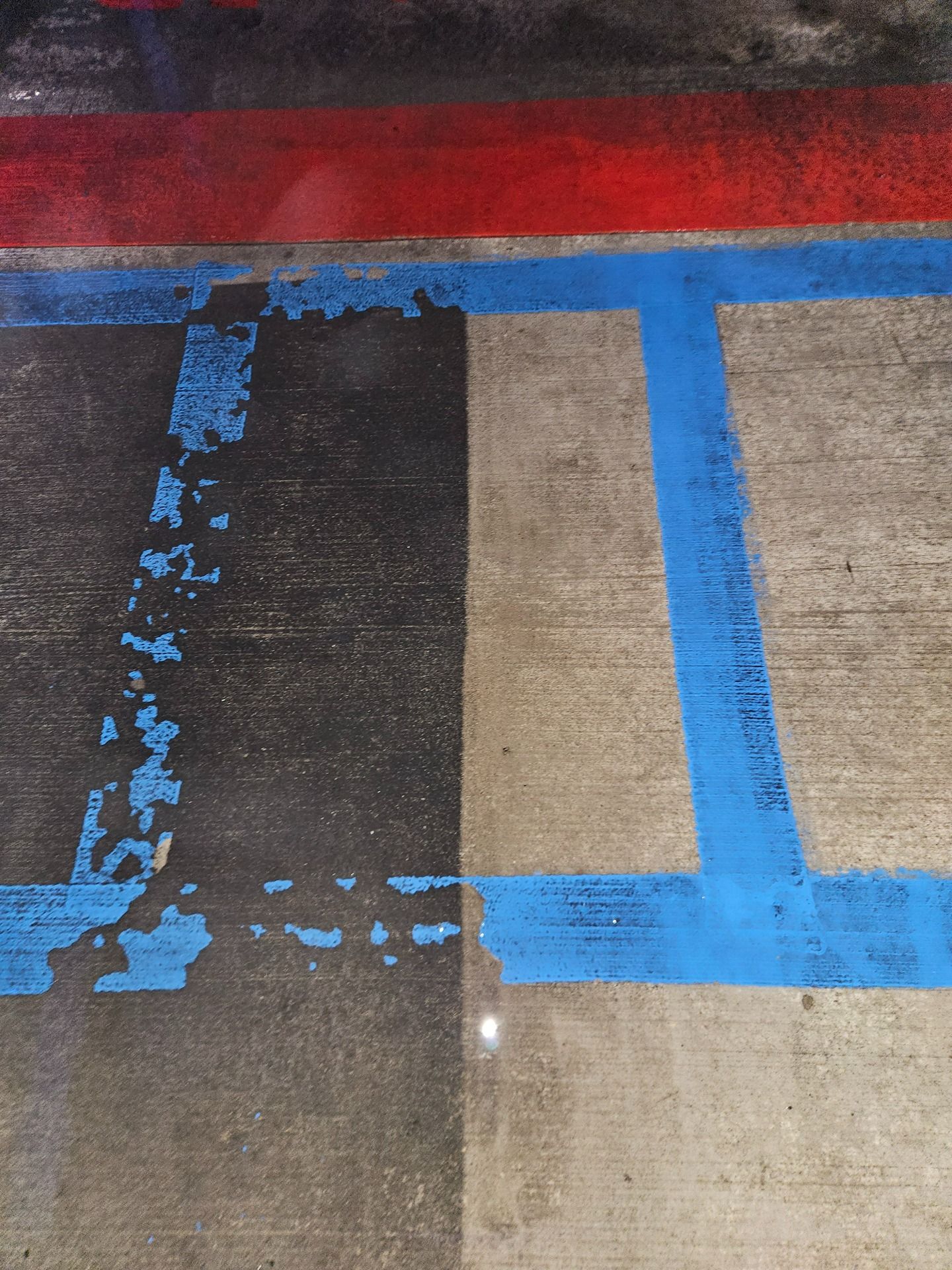 Concrete ground showing faded blue parking stripes and a red painted border line.