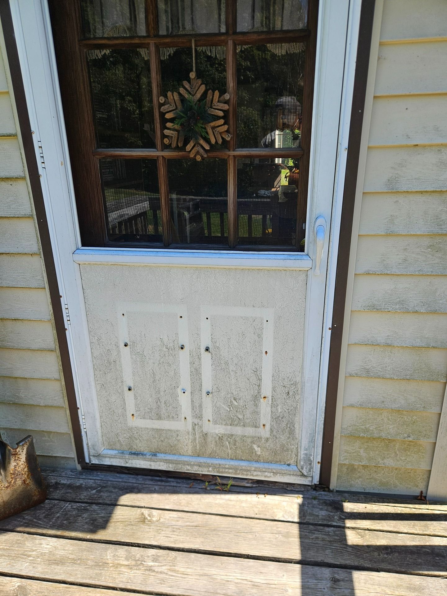 A white storm door with a snowflake decoration on the glass, featuring a bottom section covered by two white panels.