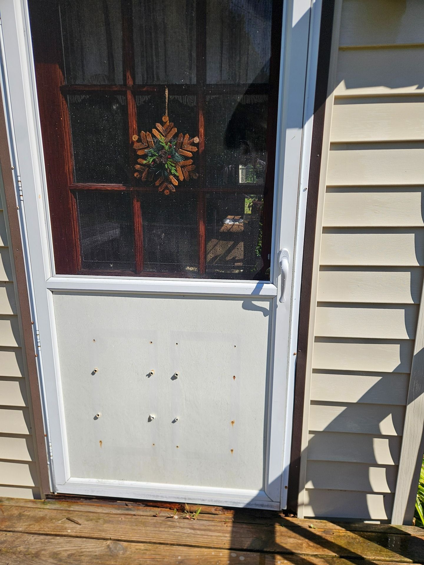 A white storm door with a glass pane, a decorative wooden snowflake, and a lower solid panel on a beige siding home exterior.