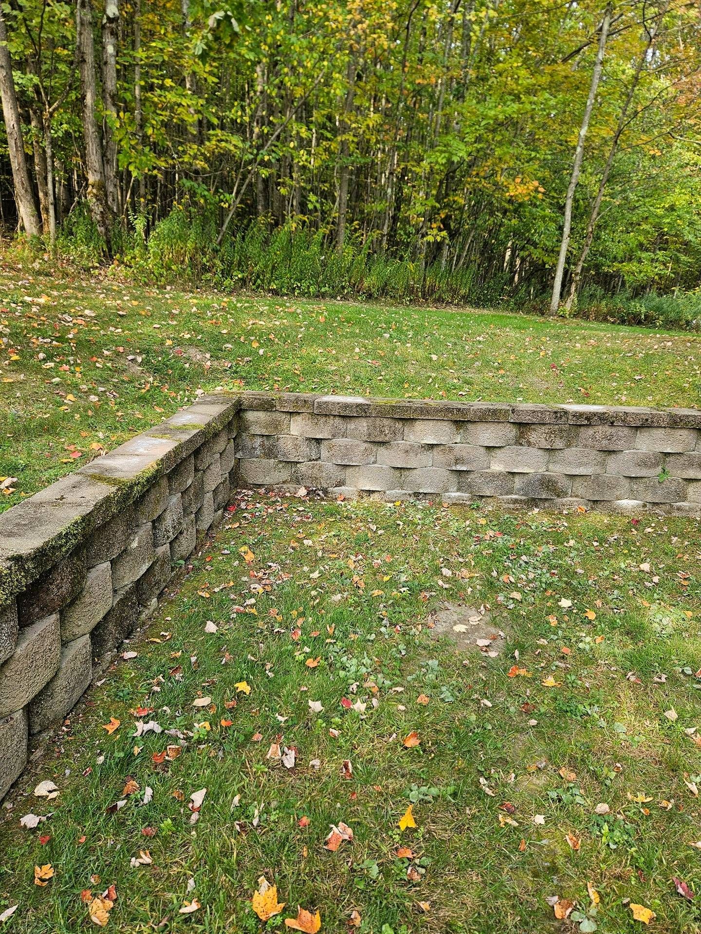 A grey stone retaining wall built into a grassy hillside surrounded by autumn trees.