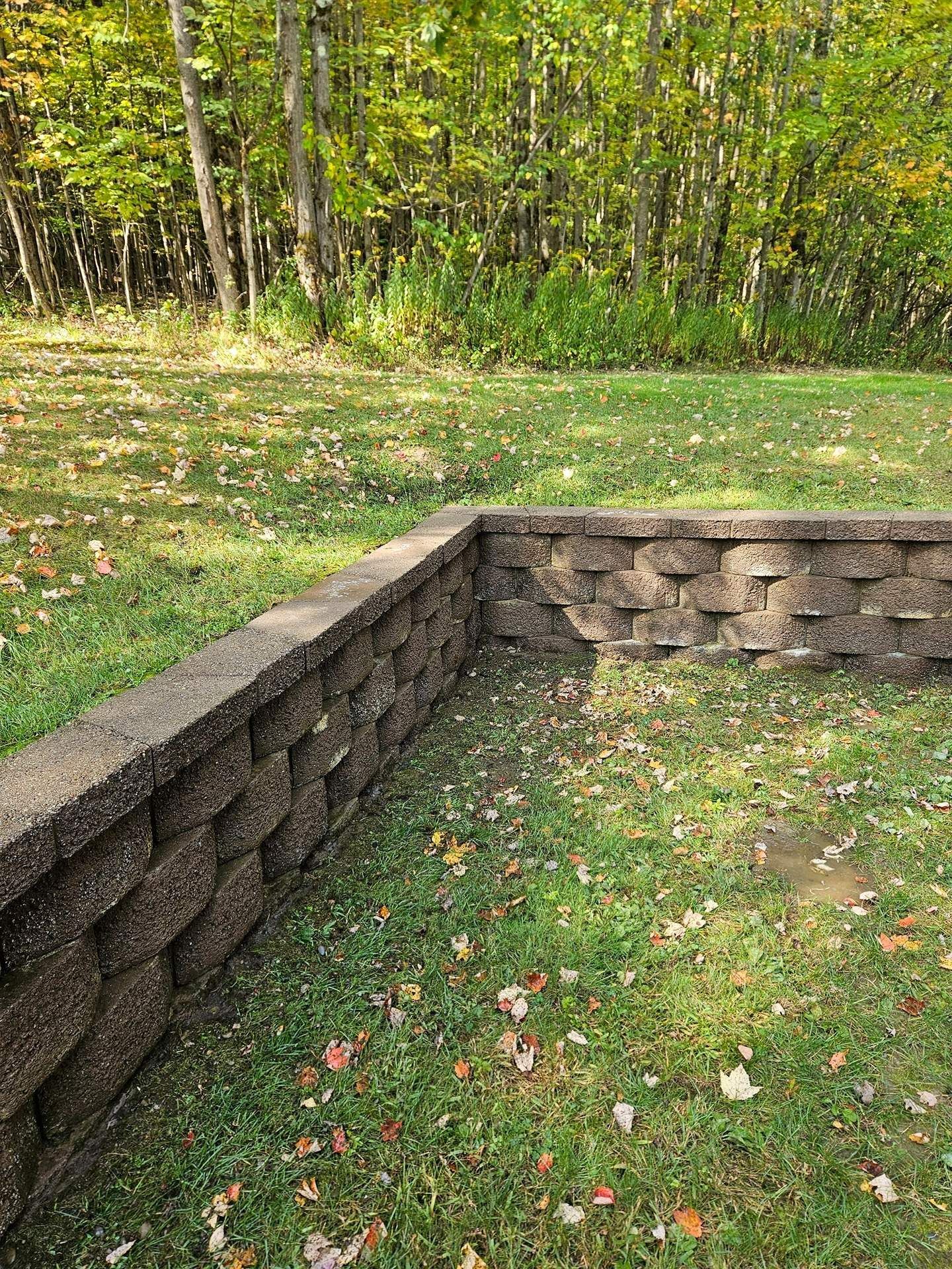 A low, L-shaped retaining wall made of stacked grey blocks on a grassy lawn with trees in the background.