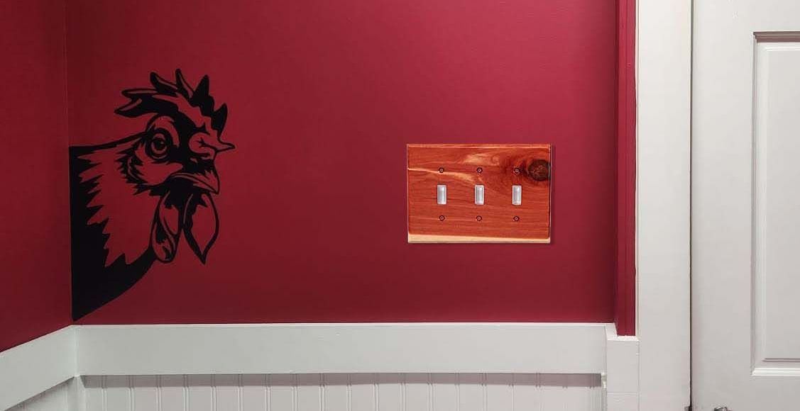 A red wall with a rooster and a traditional wood 3 toggle light switch in Tennessee Aromatic Cedar.