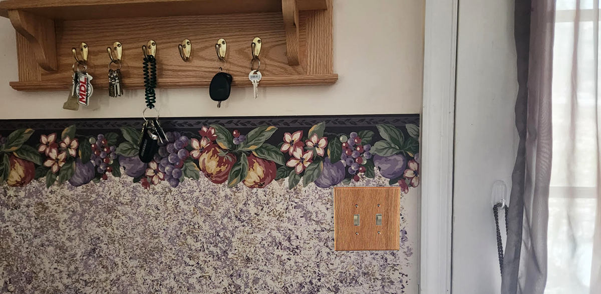 A bunch of keys are hanging on a wooden shelf with light switch plate