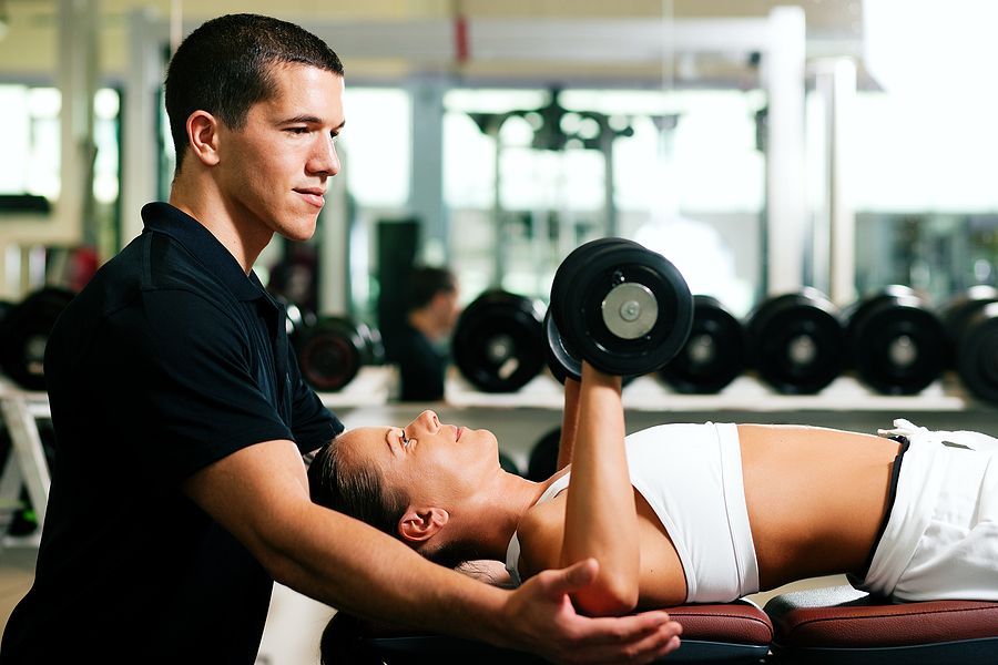 Een man helpt een vrouw met het tillen van een halter in de sportschool.