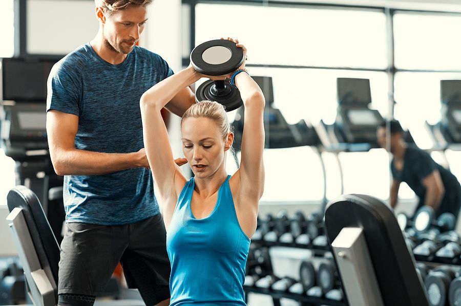 Een man helpt een vrouw met het tillen van een halter in de sportschool.
