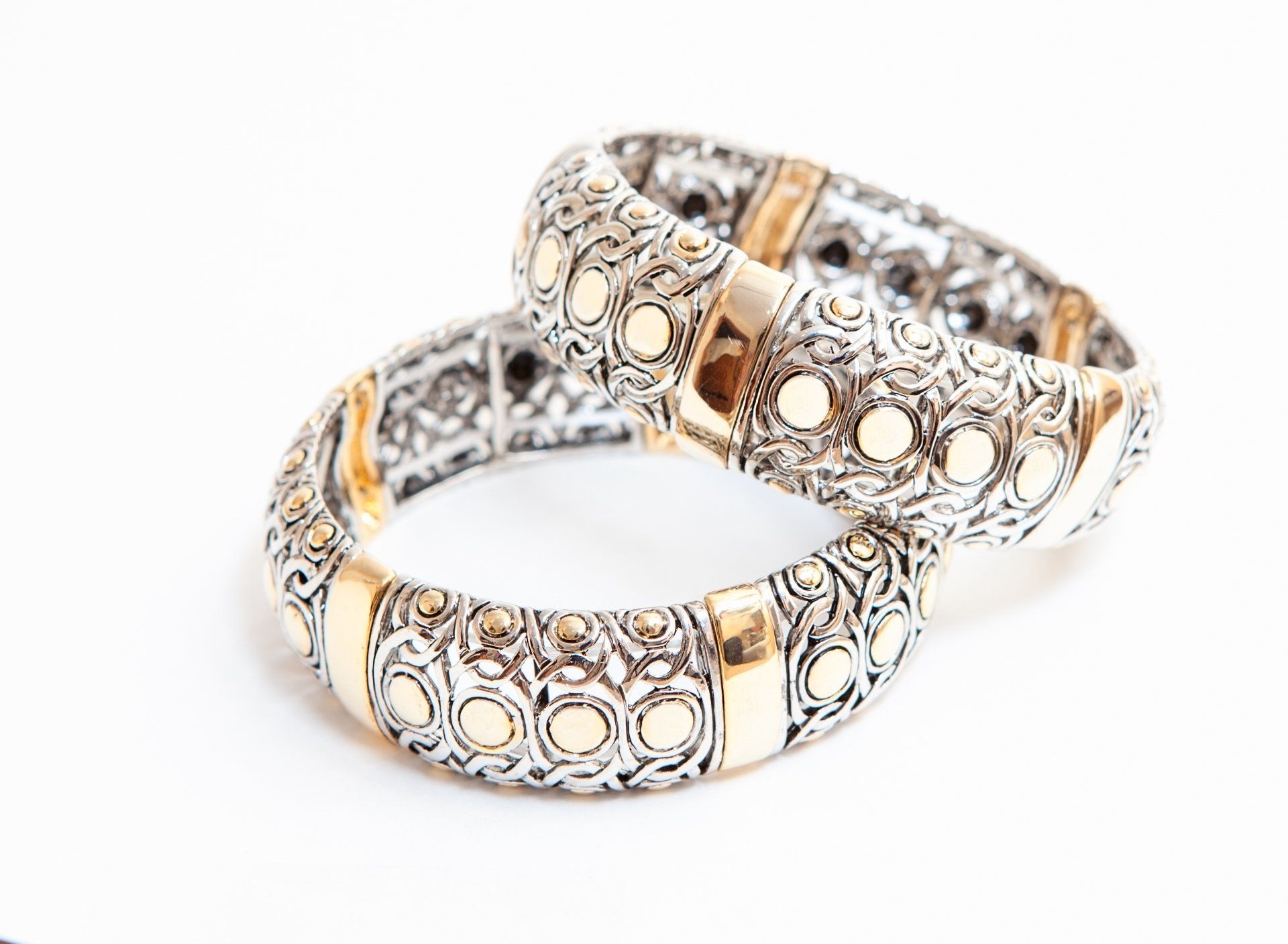 Two silver and gold bracelets are stacked on top of each other on a white surface.