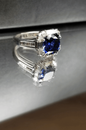 A sapphire and diamond ring is reflected in a mirror