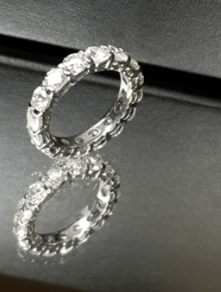 A silver ring with diamonds sits on a black surface