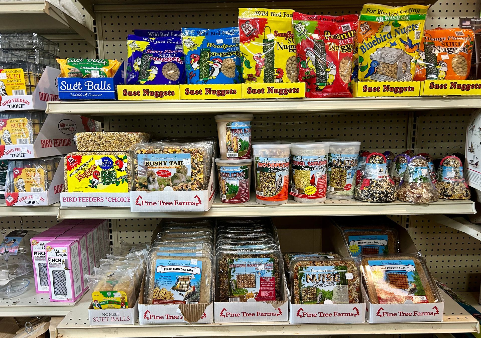 Shelves stocked with various pet food bags and containers, primarily for birds, in a store setting.