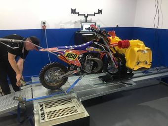 A man is working on a dirt bike on a dyno machine