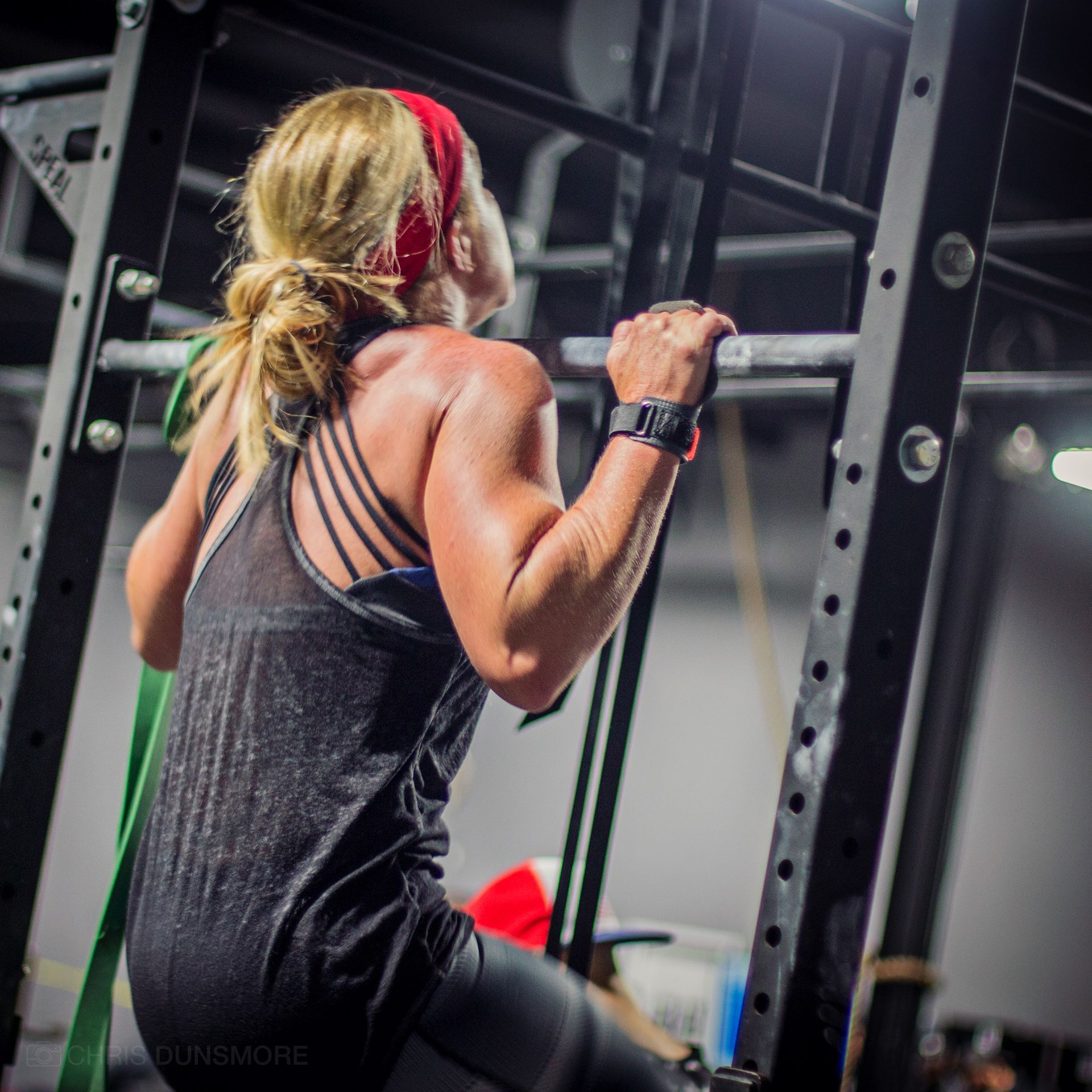 Person on a gym floor using a black foam roller, with exercise equipment and graffiti wall in the background at Resurgence Strength in Naperville, IL
