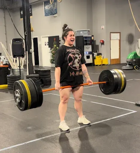 Person lifting a heavily loaded barbell in an indoor gym, mid-deadlift, with a strained expression at Resurgence Strength in Naperville, IL