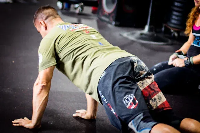 Person doing a floor push-up on a gym mat, wearing a green shirt and black shorts, with another person nearby at Resurgence Strength in Naperville, IL