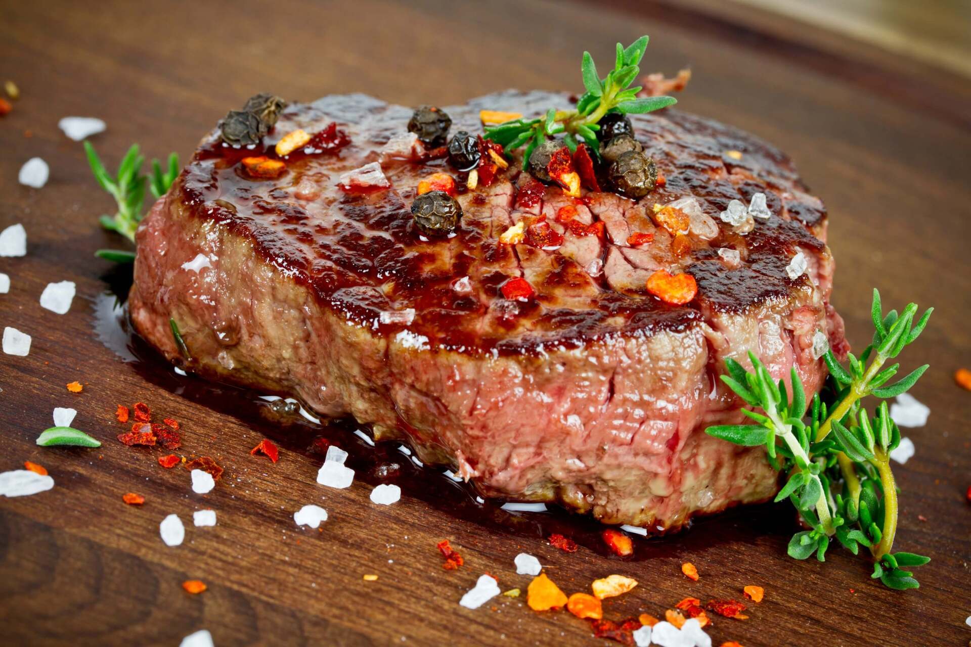 Bistecca scottata su un tagliere di legno, guarnita con erbe aromatiche, sale e pepe.