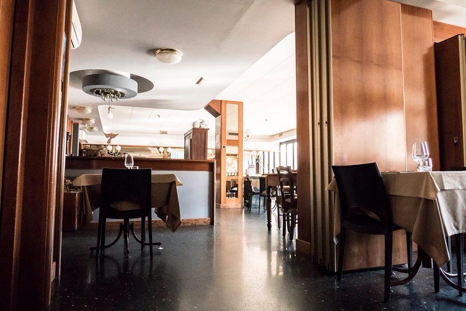 Interno di un ristorante con tavoli, sedie, pannelli in legno scuro e un pavimento nero lucido.