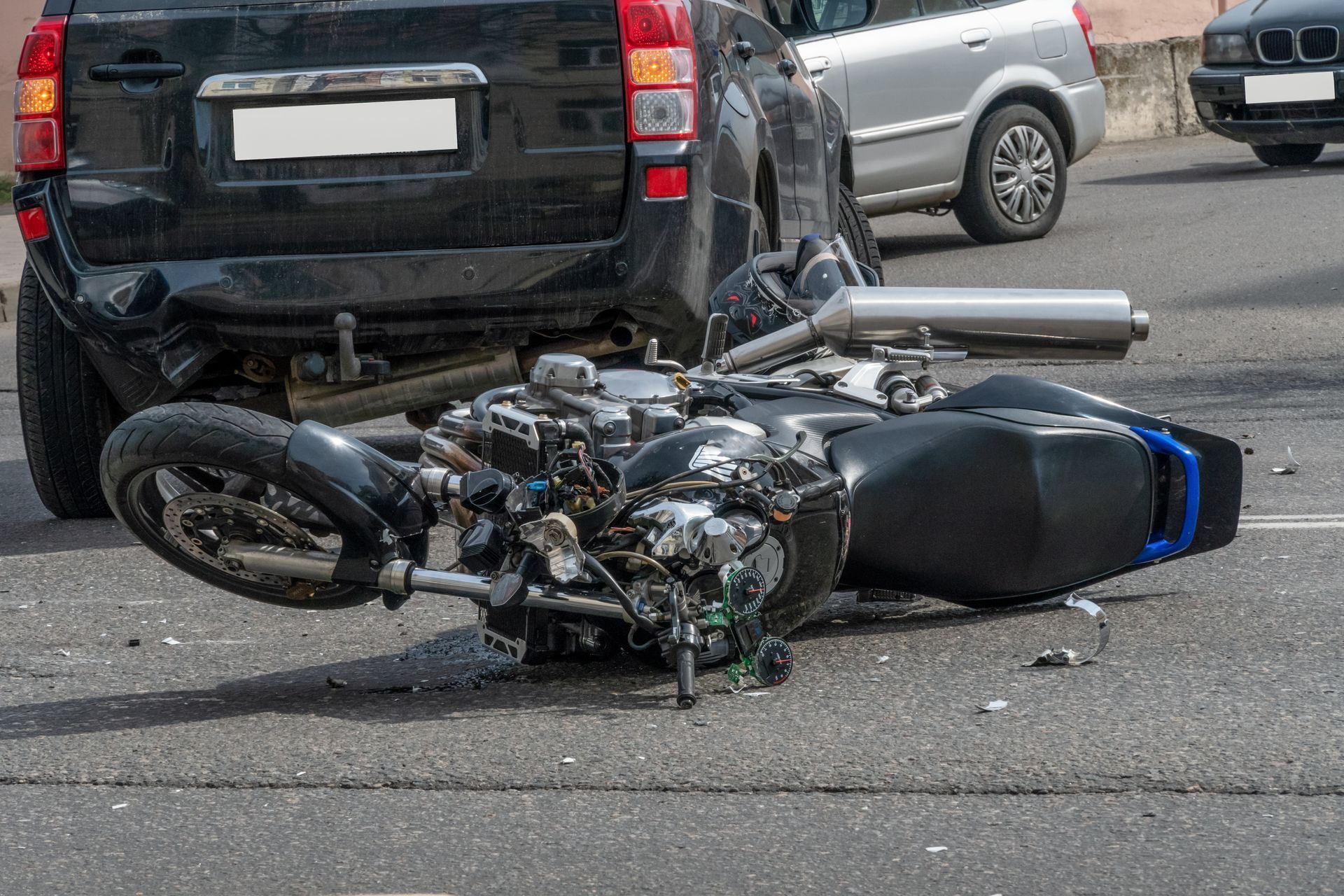 A damaged motorcycle down on the road beside an SUV after a crash.