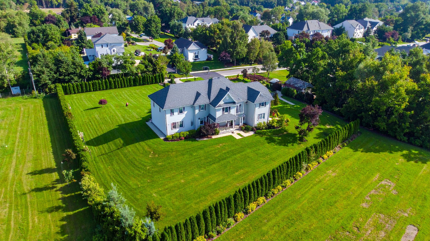 Aerial view of a white house with a large green lawn and trees in a suburban neighborhood