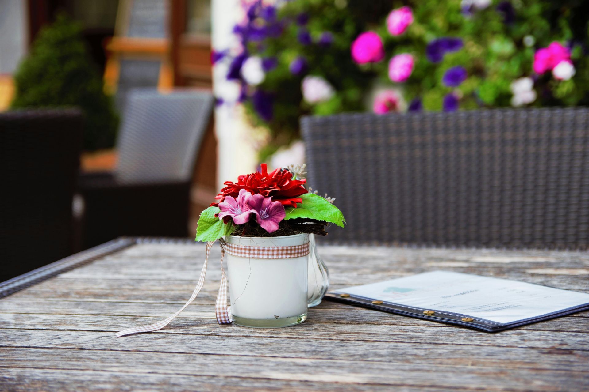 Flower arrangement on a weathered wooden table at outdoor cafe.